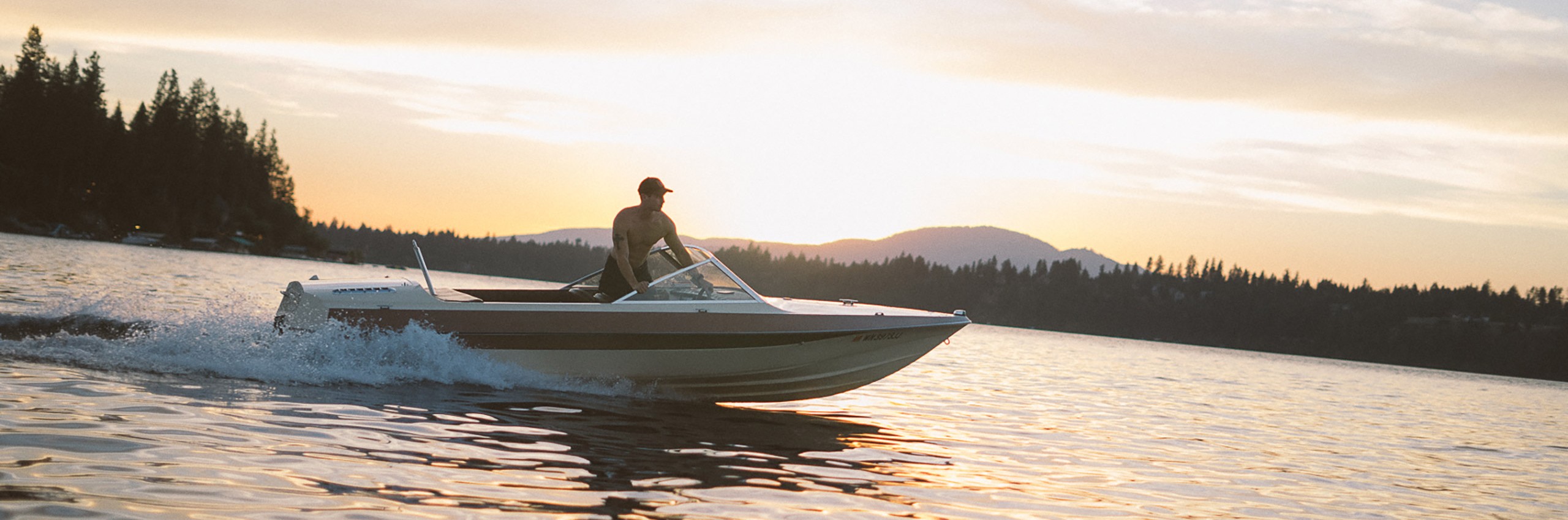 A man driving a boat on Priest Lake at sunset